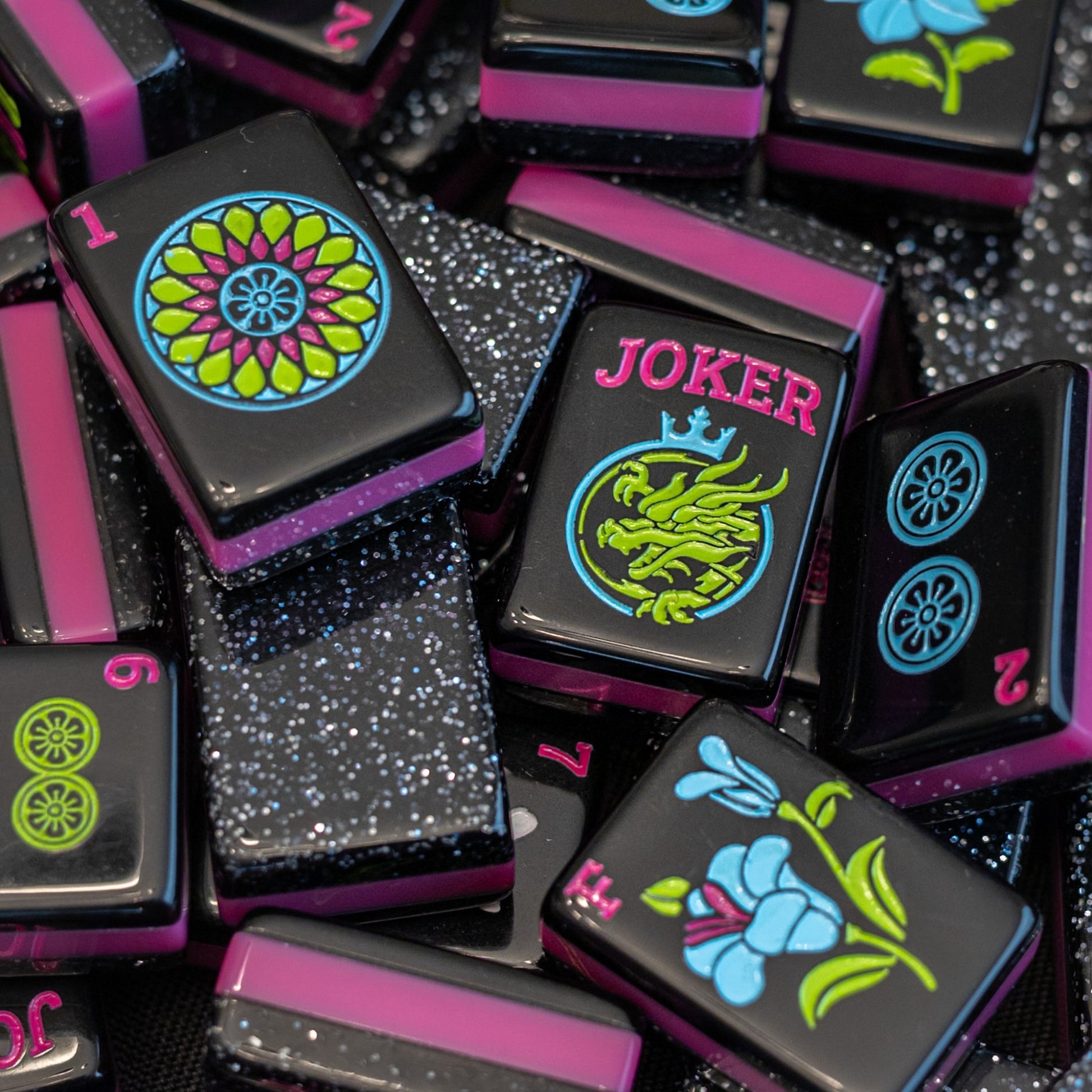 An image of a jumble of tiles from the Neon Daze tile line from Mahj Queen™.  It highlights the fun bold colors of the tiles, glittery top layer, and unique tile artwork.