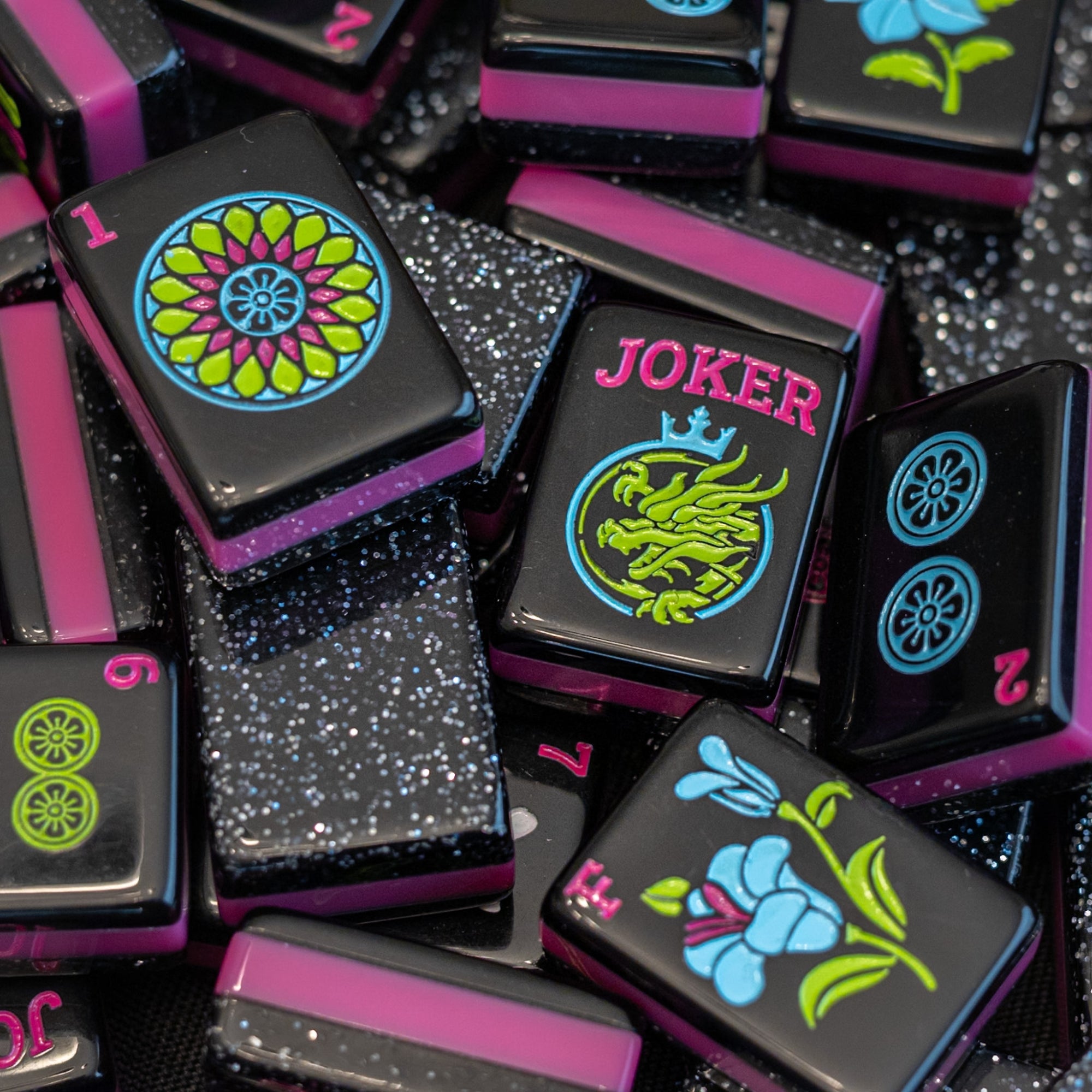 An image of a jumble of tiles from the Neon Daze tile line from Mahj Queen™.  It highlights the fun bold colors of the tiles, glittery top layer, and unique tile artwork.
